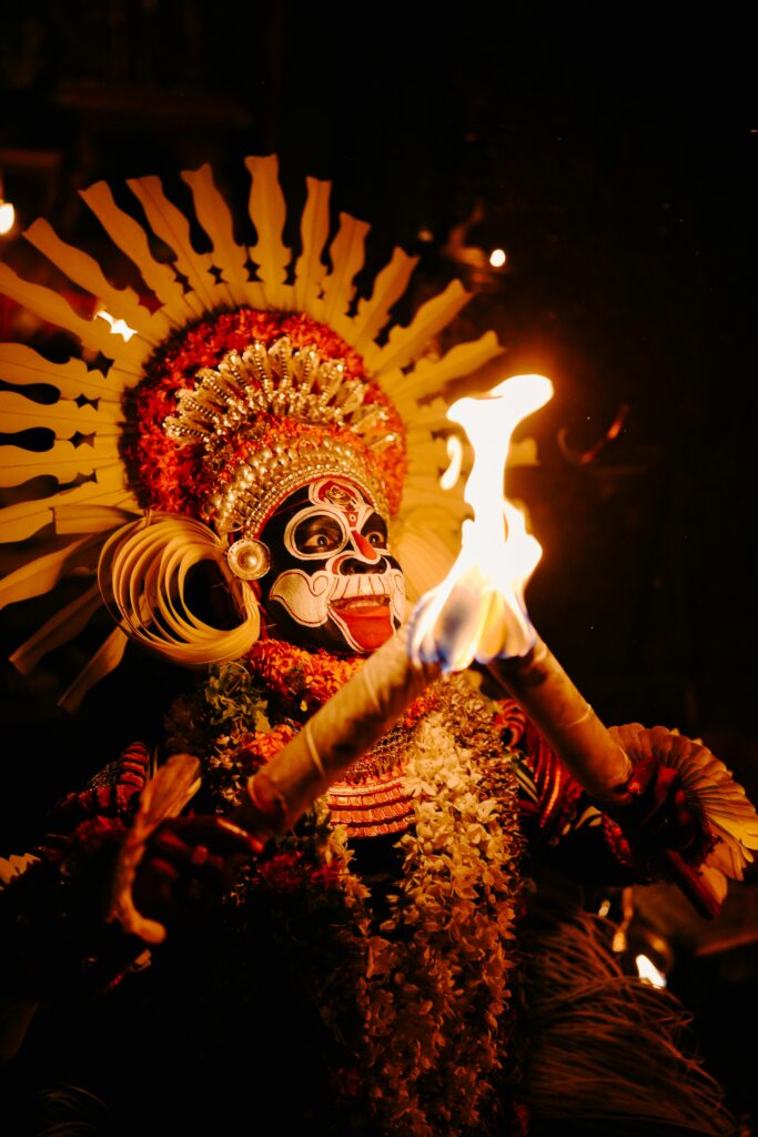 A vibrant Theyyam performer holding fire torches during a night ritual in Kannur, Kerala, India.